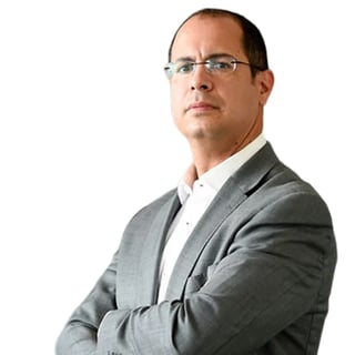 Professional headshot of a man wearing glasses and gray blazer with white shirt, arms crossed, against white background
