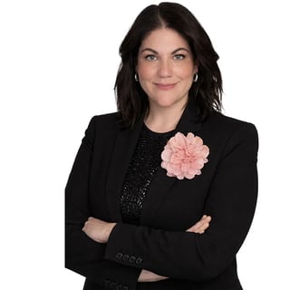 Professional headshot of a woman with black hair wearing a black blazer with a pink flower brooch