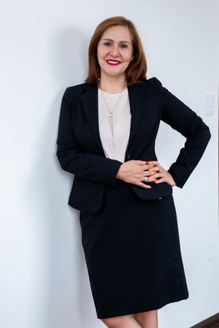 Professional woman wearing black blazer and white blouse with hand on hip, smiling at camera